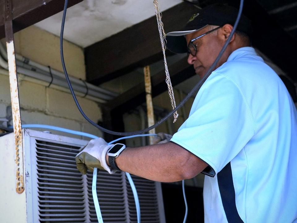 Vivek Refrigeration technician running refrigerant lines to an air conditioning unit